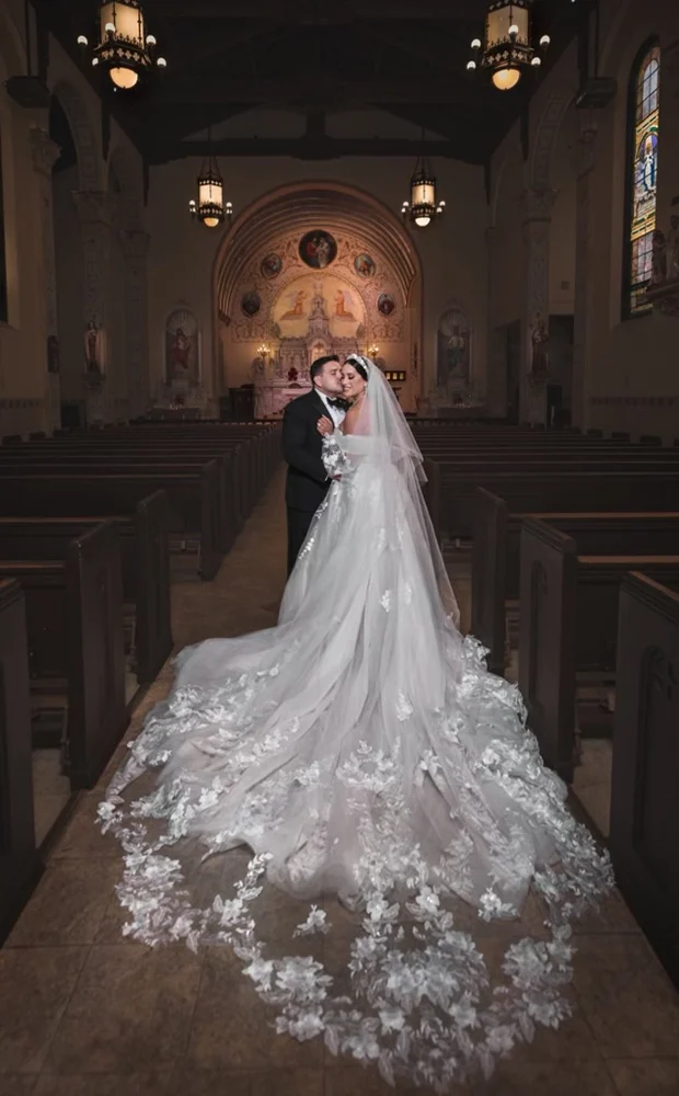 A bride and groom pose together in a church, showcasing their elegant wedding attire and the serene interior.