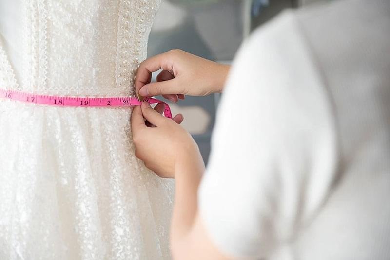 woman measuring a gown with a pink tape measure, focusing on precise fit and design details.