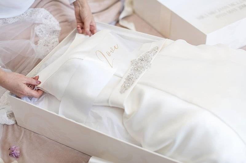 A woman carefully places a wedding dress into a decorative box, preparing it for storage or transport.