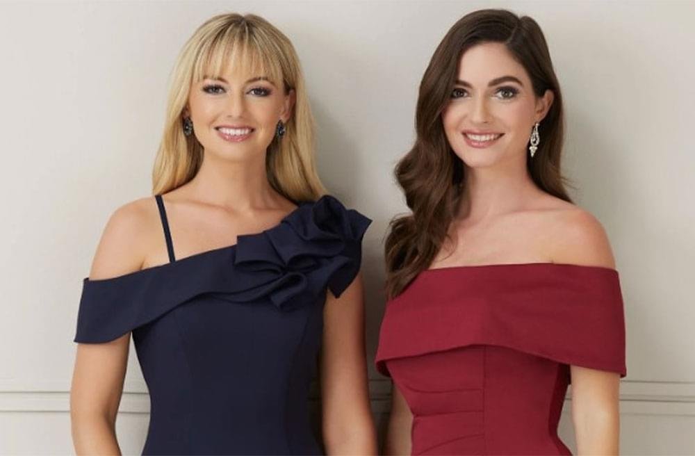 Two women in elegant red and blue gowns stand side by side, showcasing their stylish outfits.